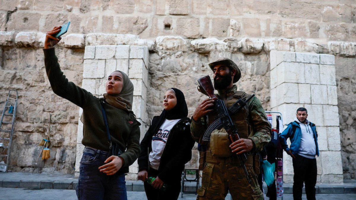 ​A woman uses a phone next to a fighter of the ruling Syrian body, after members of the ruling Syrian body ousted Syria's Bashar al-Assad, in the Damascus old city, Syria, December 12, 2024. 