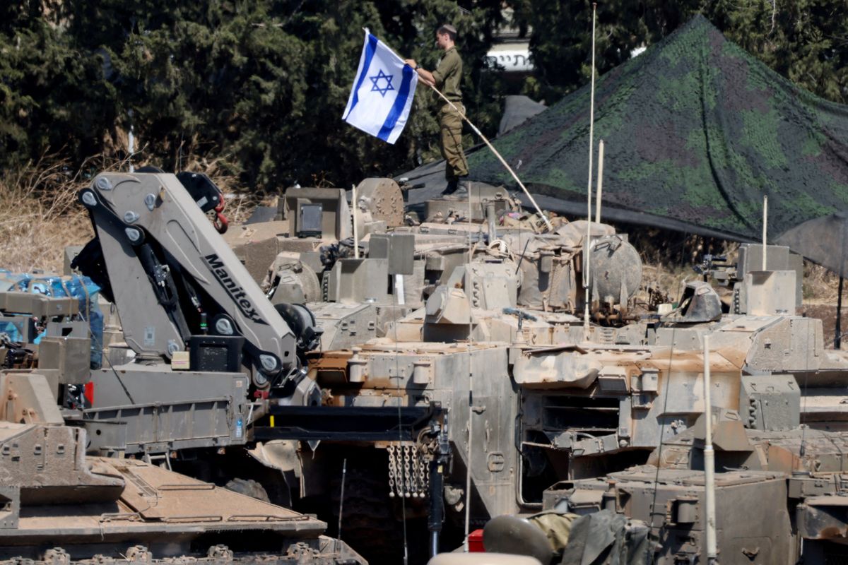 ​An Israeli member of the military adjusts an Israeli flag as armoured vehicles are arranged in formation, amid cross-border hostilities between Hezbollah and Israel, in northern Israel, September 30, 2024. 