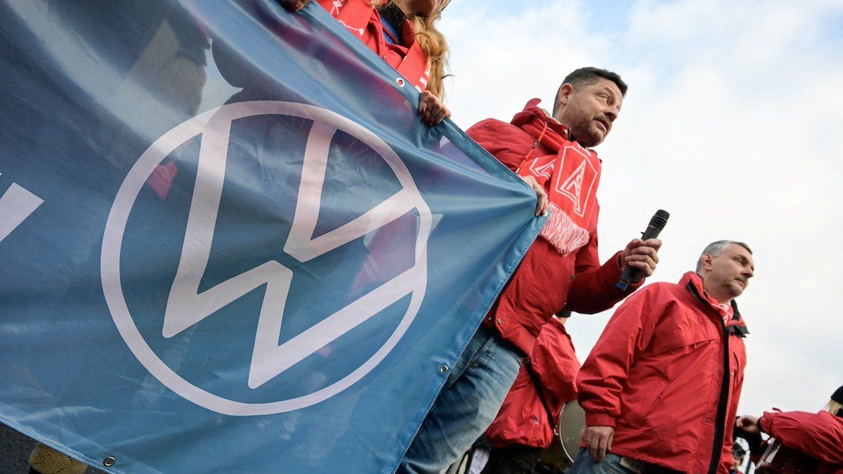 ​FILE PHOTO: A man wearing an IG Metall (Industrial Union of Metalworkers) scarf holds a banner with the Volkswagen logo, as workers gather to strike against planned cuts to wages and possible factory closures, in Hanover, Germany, December 2, 2024. Picture taken with long exposure. 