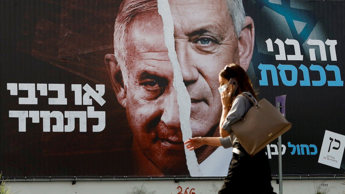 ​FILE PHOTO: A woman walks past a Blue and White party election campaign banner depicting its leader, Israeli Defence Minister Benny Gantz, alongside Israeli Prime Minister Benjamin Netanyahu ahead of the March 23 ballot, in Tel Aviv, Israel March 14, 2021. 
