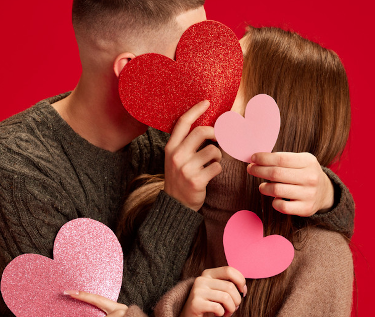 ​Happy young couple hide behind paper hearts to kiss.