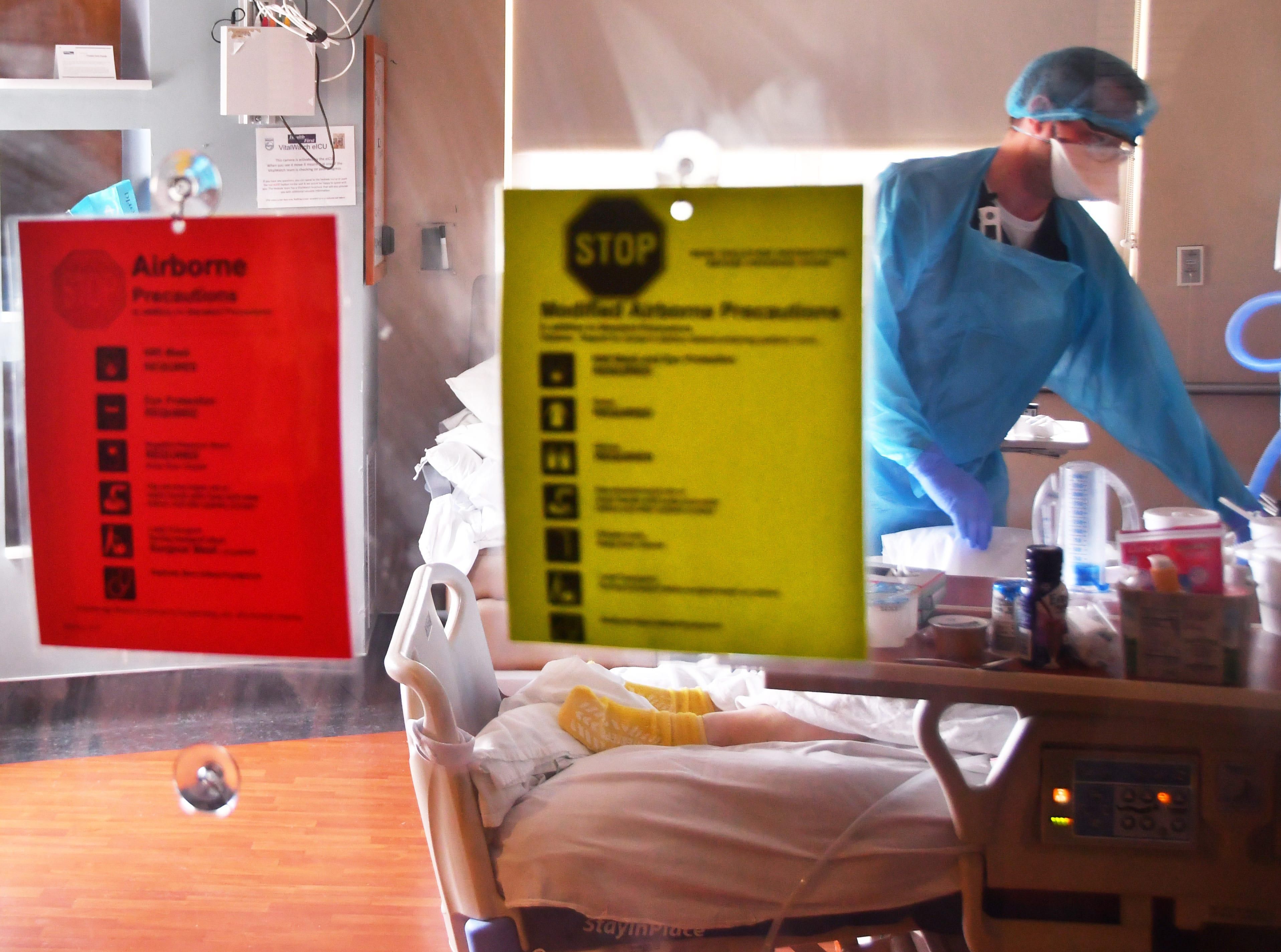 Seen through a protective glass door, Dustin Evans, a critical care nurse, attends to a COVID-19 patient in the intensive care unit on the fourth floor of Holmes Regional Medical Center in Melbourne, Fla., on May 12.