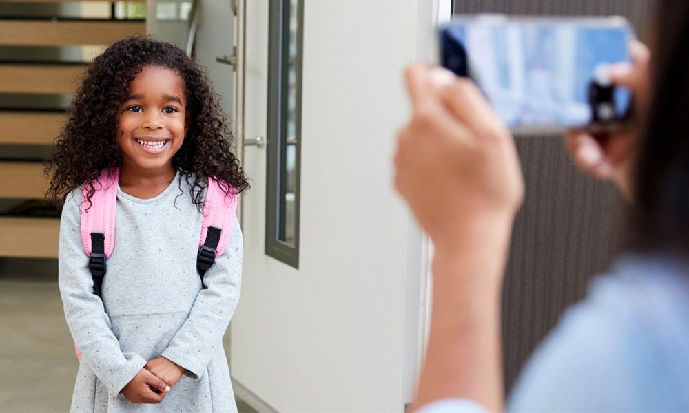 A small curly haired girl child with a school bag smiling for a photograph