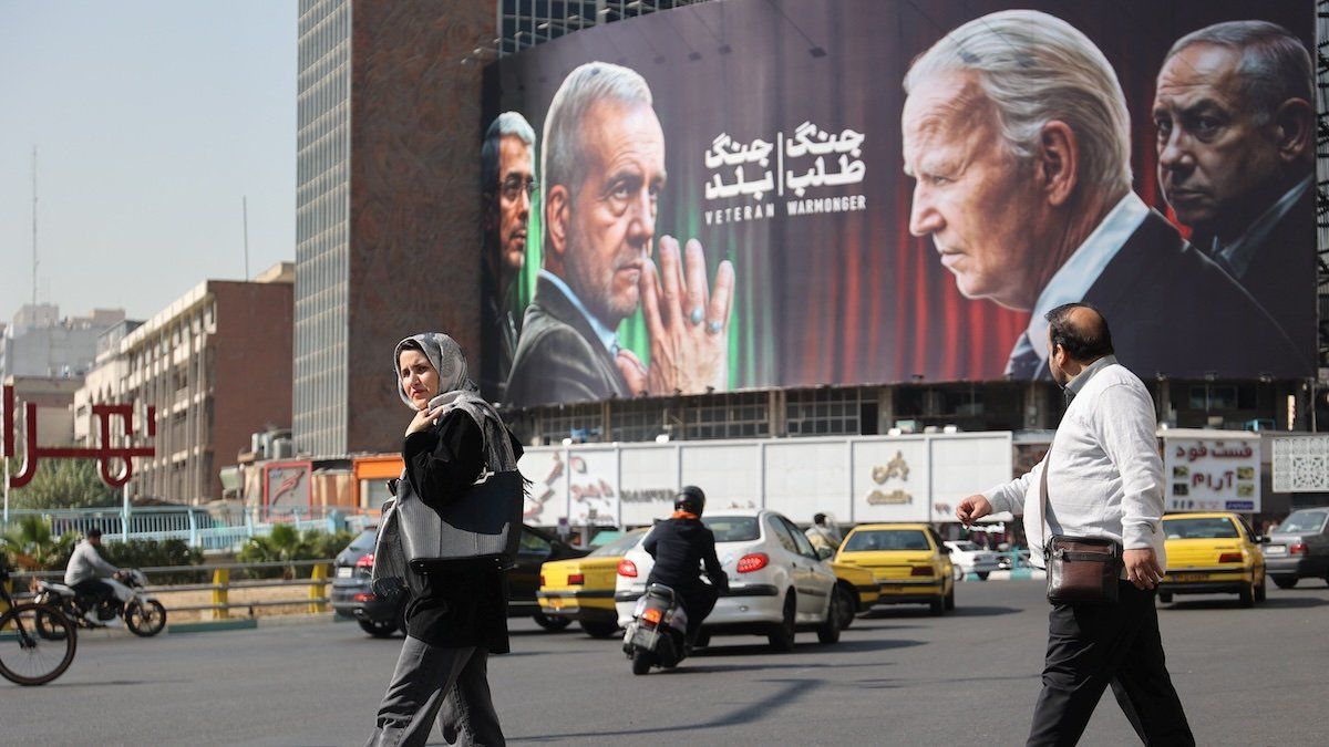 ​Iranians walk next to an anti-US and Israeli billboard with pictures of Iranian President Masoud Pezeshkian and Iranian Armed Forces Chief of Staff, Major General Mohammad Bagheri, and US President Joe Biden and Israeli Prime Minister Benjamin Netanyahu, on a street in Tehran, Iran, October 27, 2024.