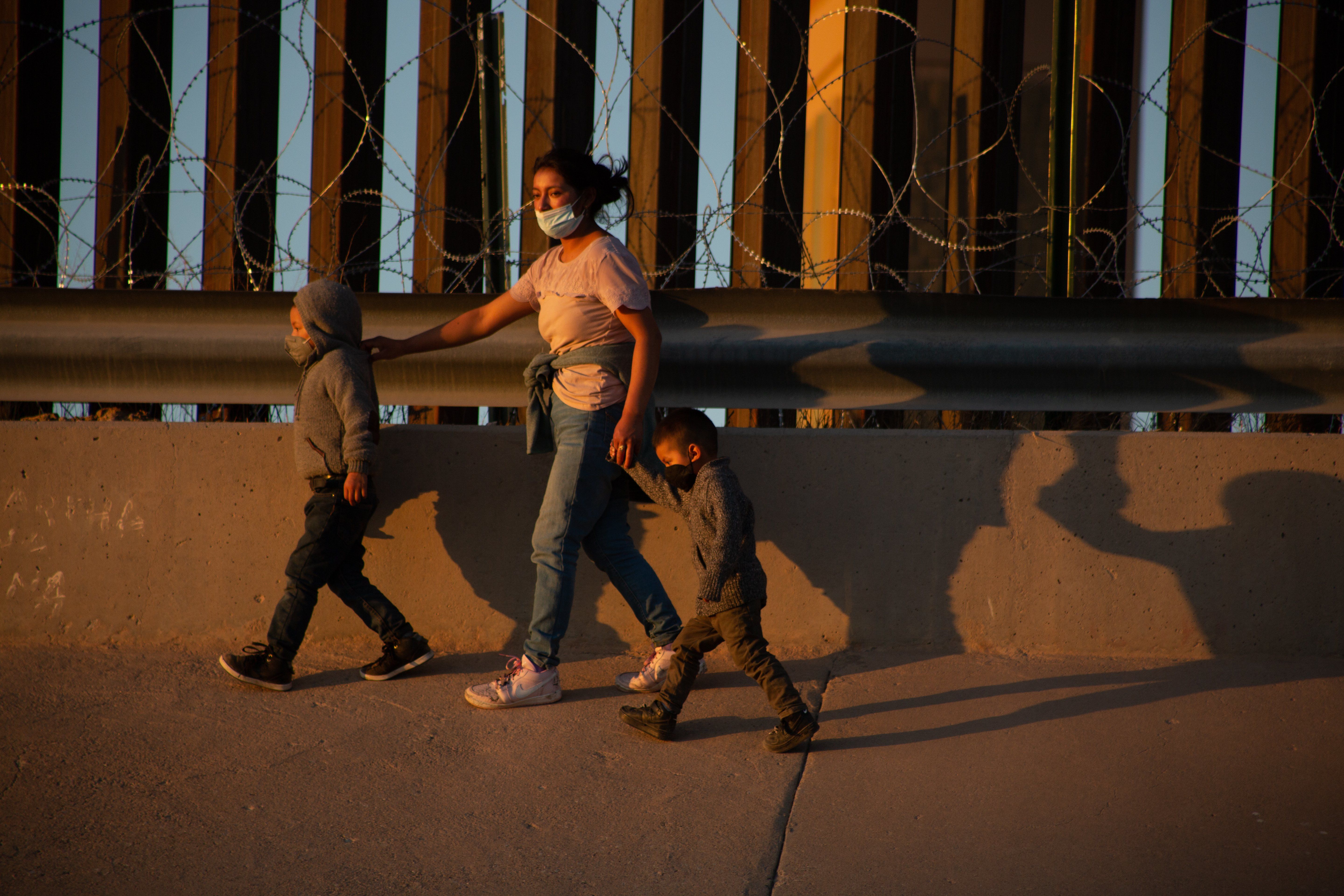 A mother and her two children walk to one side of the United States wall after crossing the Rio Grande.