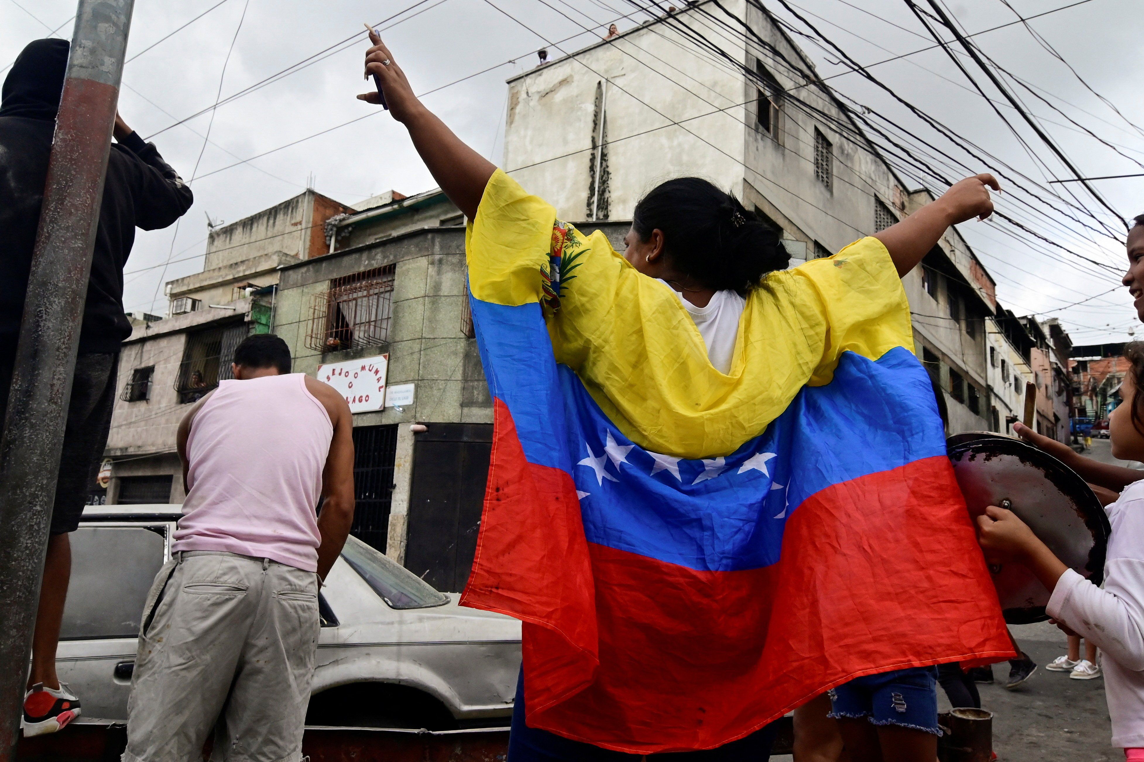 ​A woman wears a Venezuela flag as other resident bangs a pot to protest against the election results after both President Nicolas Maduro and his opposition rival Edmundo Gonzalez claimed victory in Sunday's presidential election at Los Magallanes de Catia neighborhood, in Caracas, Venezuela July 29, 2024. 