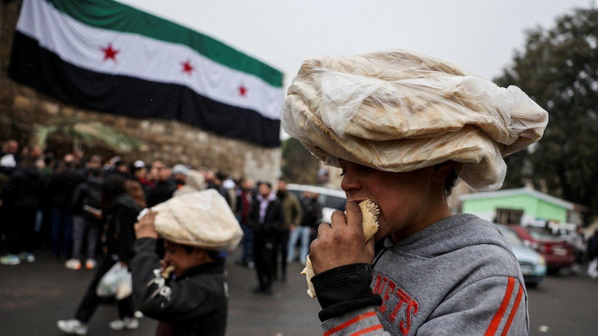 ​FILE PHOTO: Children eat bread on a street near a flag adopted by the new Syrian rulers, after the ousting of Syria's Bashar al-Assad, in Damascus, Syria, December 24, 2024. 