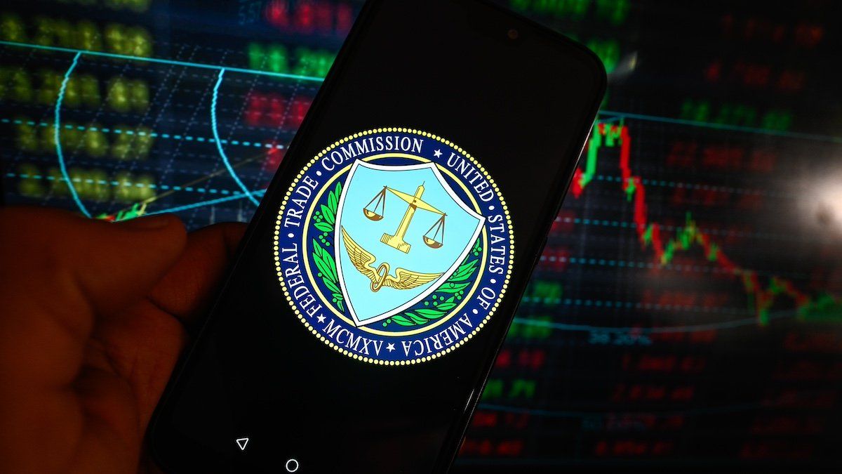 In this photo illustration, the US Federal Trade Comission logo is displayed on a smartphone with stock market percentages in the background.