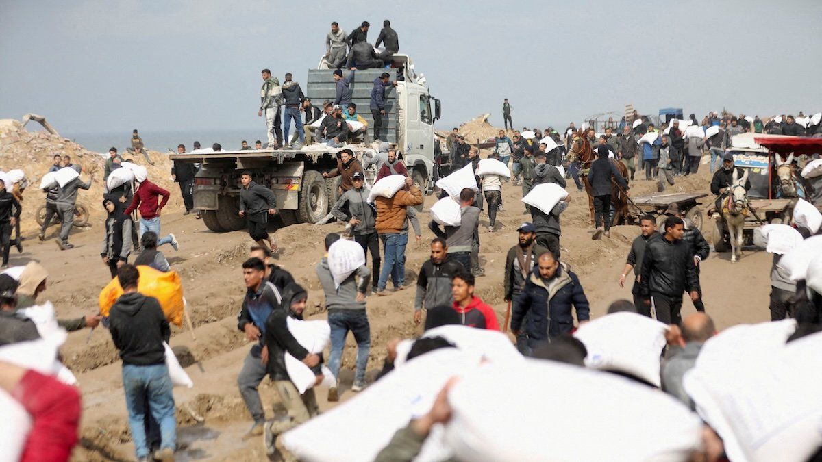 ​Palestinians carry bags of flour they grabbed from an aid truck near an Israeli checkpoint in Gaza City, February 19, 2024.