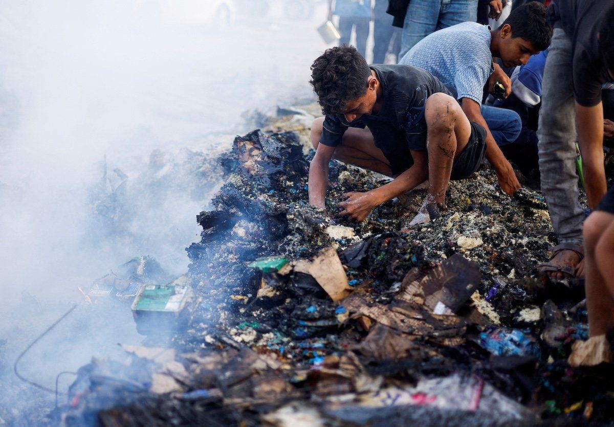 ​Palestinians search for food among burnt debris in the aftermath of an Israeli strike on an area designated for displaced people, in Rafah in the southern Gaza Strip, on May 27, 2024. 