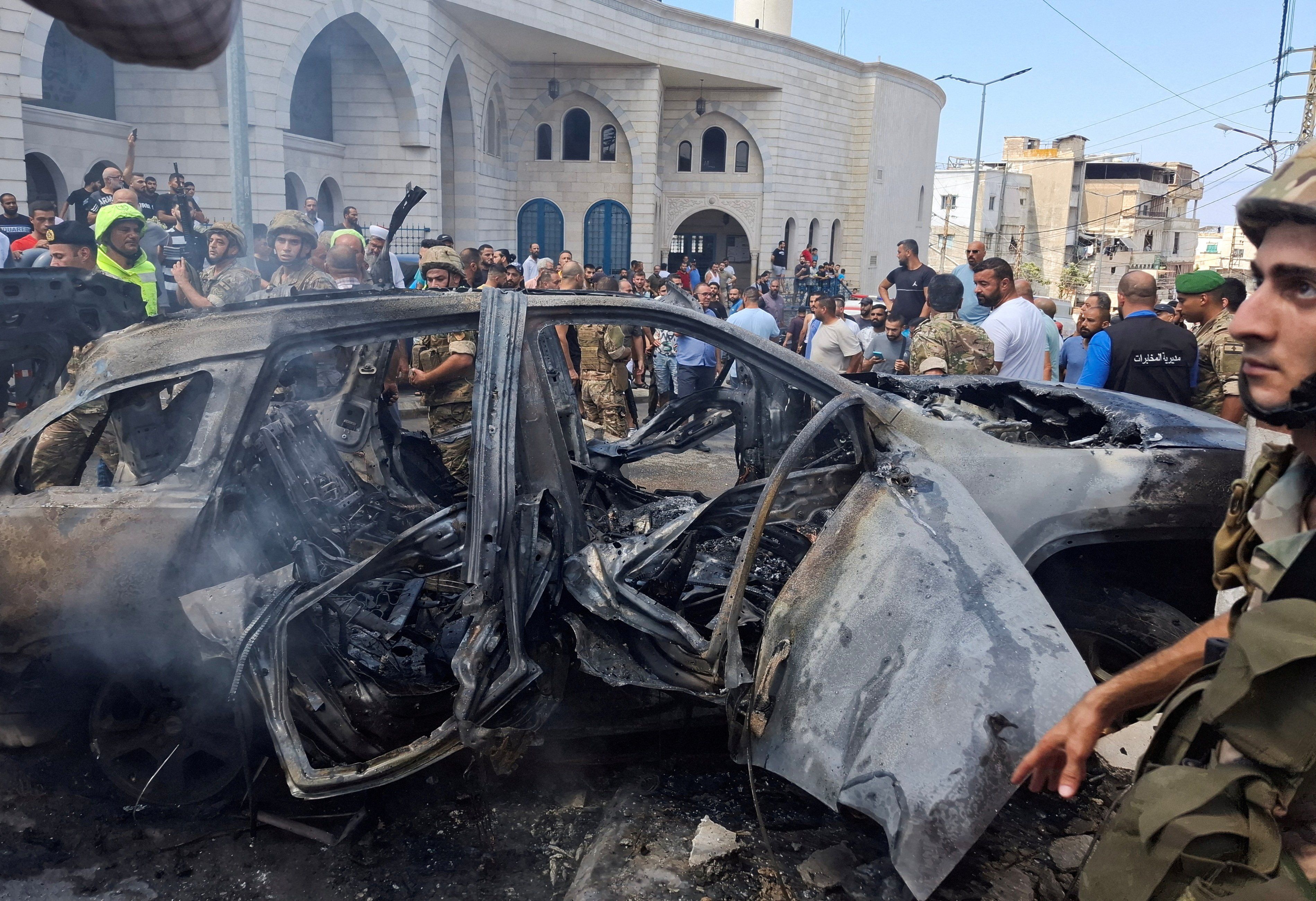 People and Lebanese army members stand near a burnt car after an Israeli strike on the outskirts of the southern port city of Sidon, according to two Palestinian sources, in Lebanon August 21, 2024. 