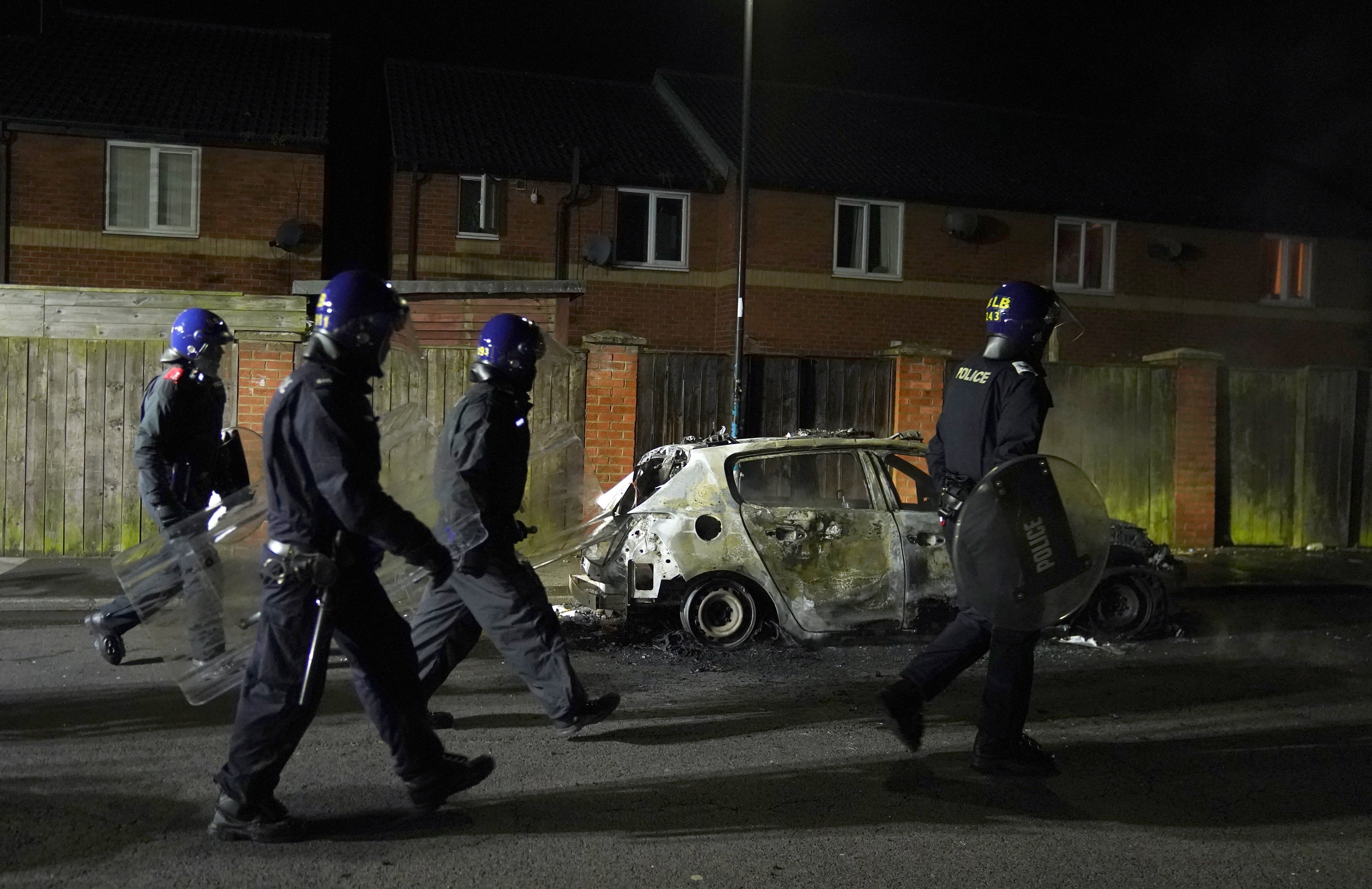 Police Officers walk past a burnt out police vehicle as they are deployed on the streets of Hartlepool following a violent protest. 