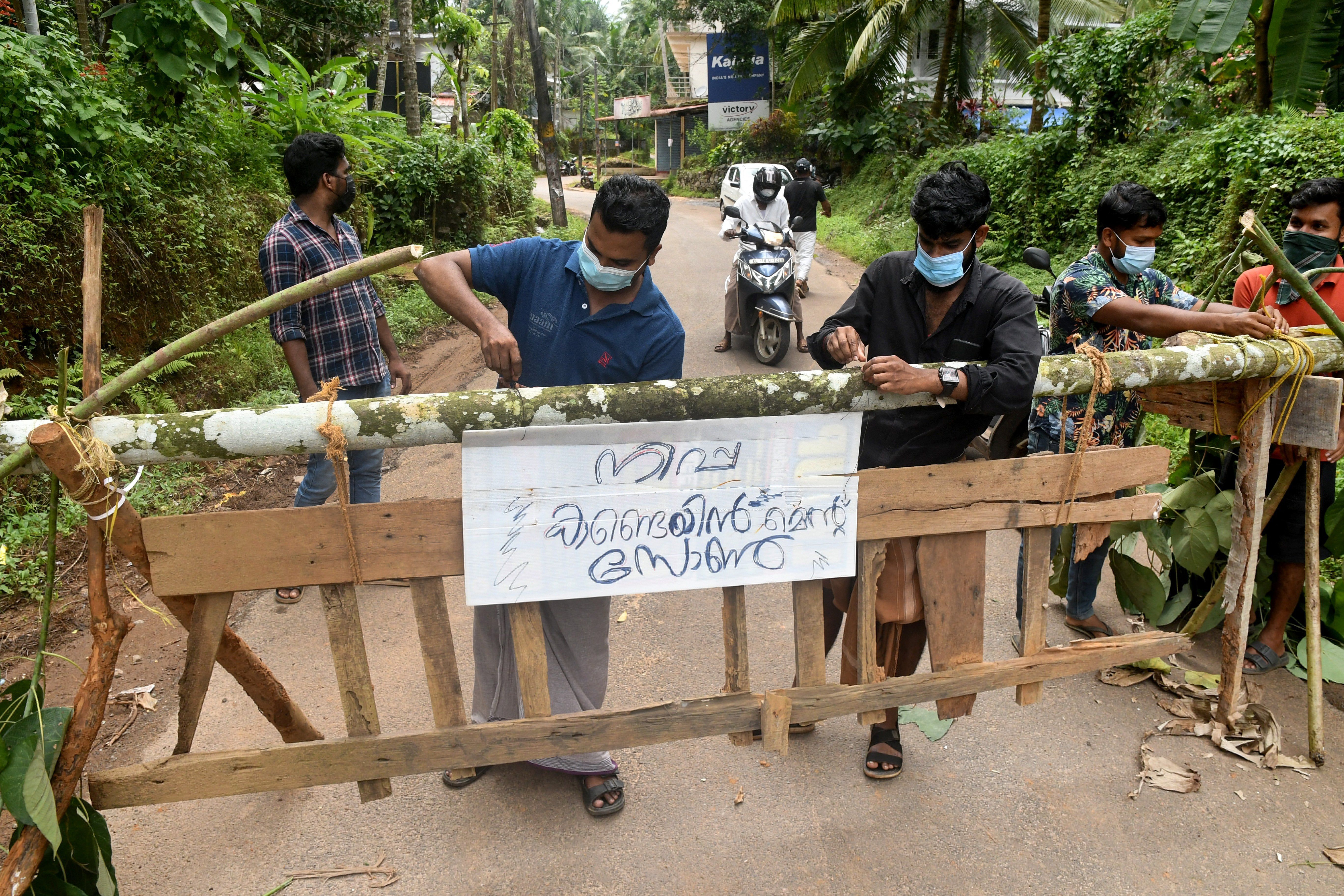 Residents fix a sign reading "Nipah containment zone" on a barricade