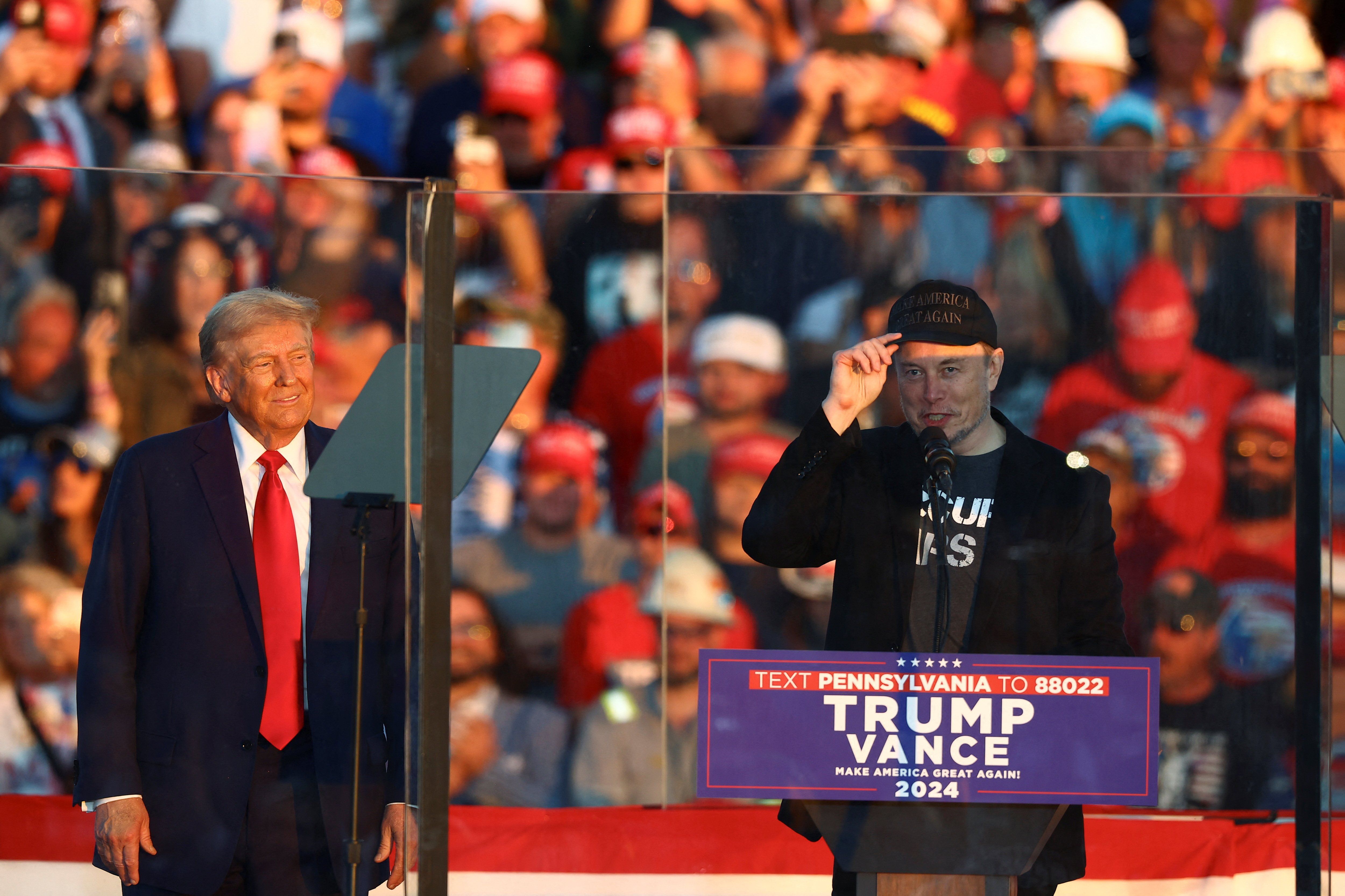 ​Tesla CEO and X owner Elon Musk speaks as Republican presidential nominee and former U.S. president Donald Trump looks on during a rally at the site of the July assassination attempt against Trump, in Butler, Pennsylvania, U.S., October 5, 2024. 