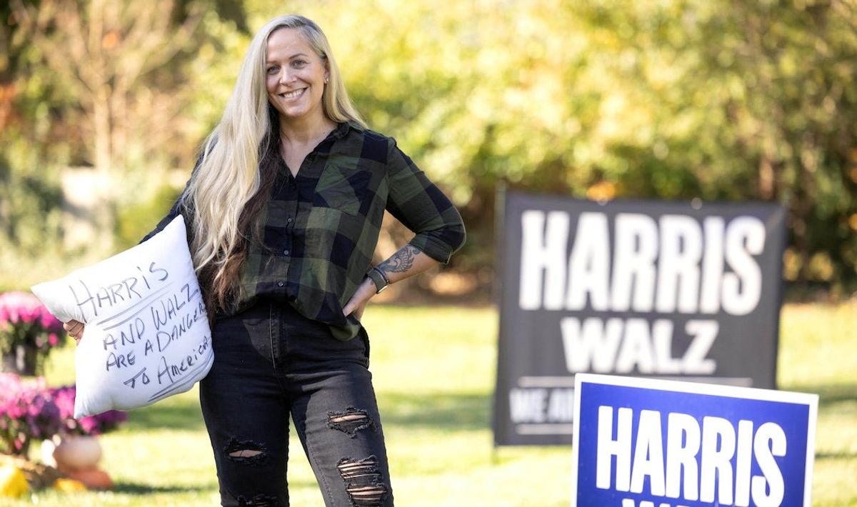 ​Lissa Smith poses with lawn signs in support of Kamala Harris, and a pillow someone threw in her yard after several signs, previously displayed on her lawn, were taken outside her home in Indianapolis, Indiana, on Oct. 27, 2024. 