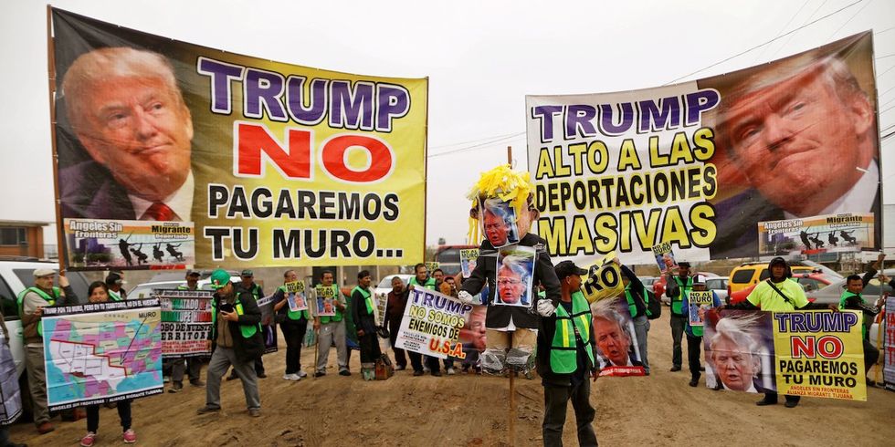 ​People hold signs reading "Trump, we will not pay for the wall" and "Trump, stop the mass deportations" near the border fence between Mexico and the U.S., in Tijuana, Mexico March 13, 2018. 