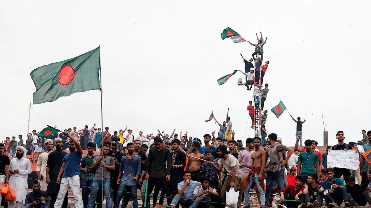 People waves Bangladeshi flags on top the Ganabhaban, the Prime Minister's residence, as they celebrate the resignation of PM Sheikh Hasina in Dhaka, Bangladesh, August 5, 2024. 