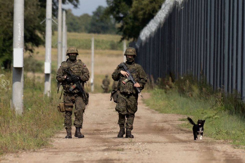 Polish soldiers and a local dog walk along the border fence on the Polish-Belarusian border in Usnarz Gorny, Poland. 
